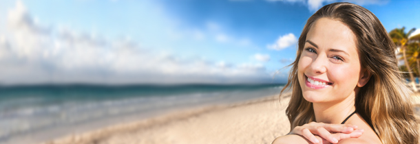 Gebräunte Haut: Eine Frau befindet sich am Strand und lächelt den Betrachter an