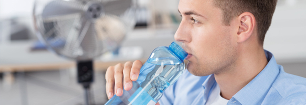 Ein junger Geschäftsmann leidet an der Hitze im Büro - er trinkt Wasser