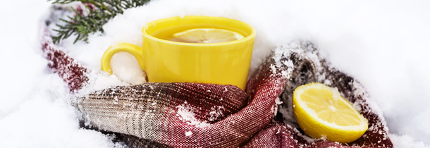 Eine Tasse Tee mit Zitronen und ein Schal liegen im Schnee
