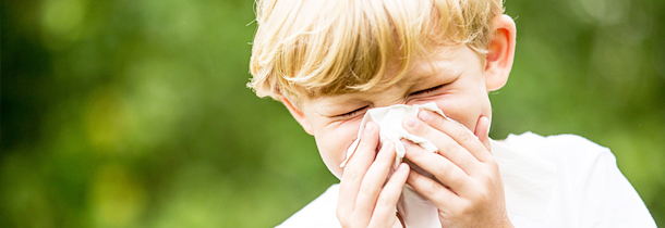 Ein Junge mit Heuschnupfen putzt sich die Nase.