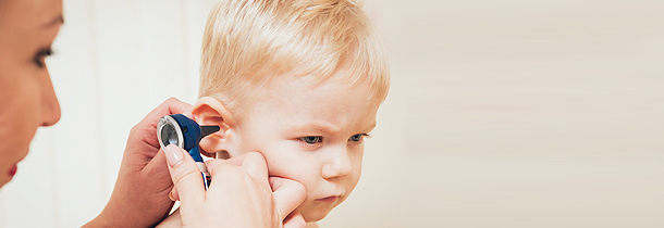 Ärztin schaut mittels Otoskop in das rechte Ohr eines jungen Knaben mit blonden Haaren