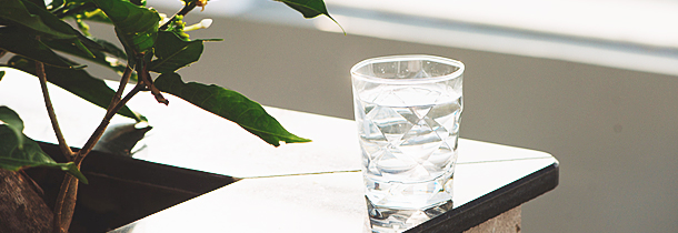 Ein Glas Wasser befindet sich auf einer Marmoroberfläche nahe einer Pflanze