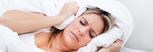 Eine Dame mit blonden Haaren liegt im Bett und leidet stark an Migräne