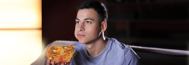 Junger Mann vor dem Fernseher am Pizza essen