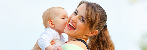 Eine junge Mutter hält ihr Baby nahe an sich und lächelt den Betrachter an