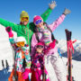 Eine junge Familie steht in Skiausrüstung vor einem Bergpanorama.