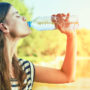 Eine blonde junge Frau trinkt Wasser aus einer Plastikflasche bei intensiver Sonneneinstrahlung