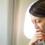 Junge Frau sitzt auf ihrem Sitz im Flugzeug und wirkt angespannt
