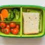 Eine grüne Pausenbox mit belegtem Brot und Gemüse wird von oben gezeigt