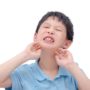 Ein kleiner asiatischer Junge hat Mumps und hält sich die Wangen mit schmerzverzerrtem Gesichtsausdruck
